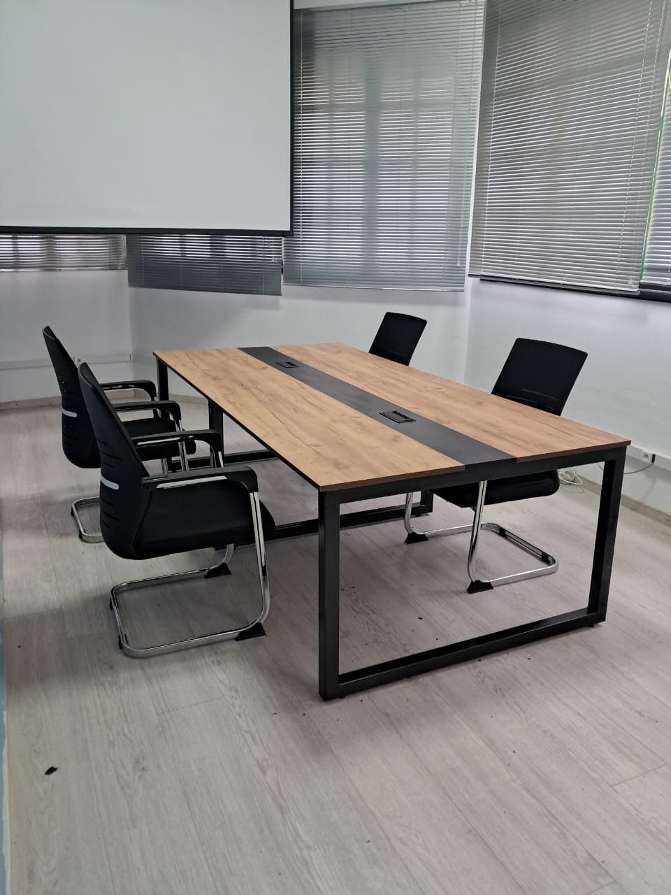 Table de réunion bois à structure métallique noire, entourée de chaises noires.